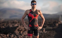 Athlete in a triathlon suit standing confidently with hands on hips against a mountainous background.