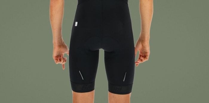 Back view of person wearing black Fase bib shorts against a green background.