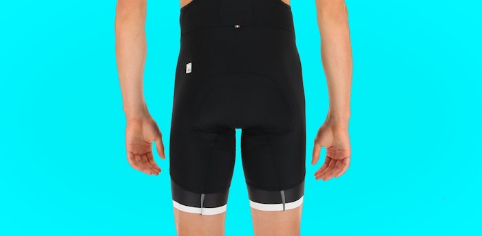 Back view of person wearing black Sleek 99 bib shorts against a bright blue background.