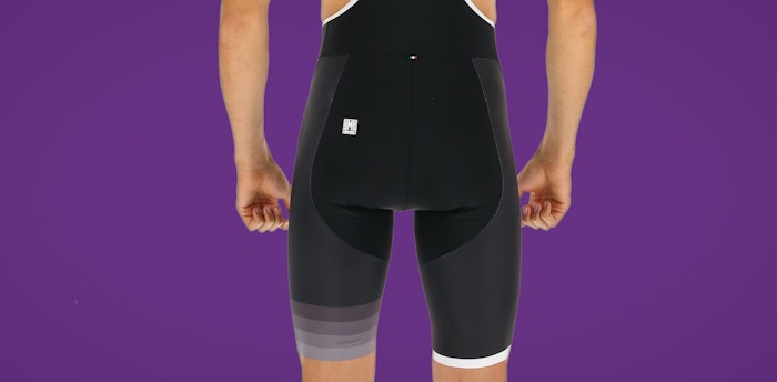 Back view of person wearing black Tono bib shorts against a purple background.