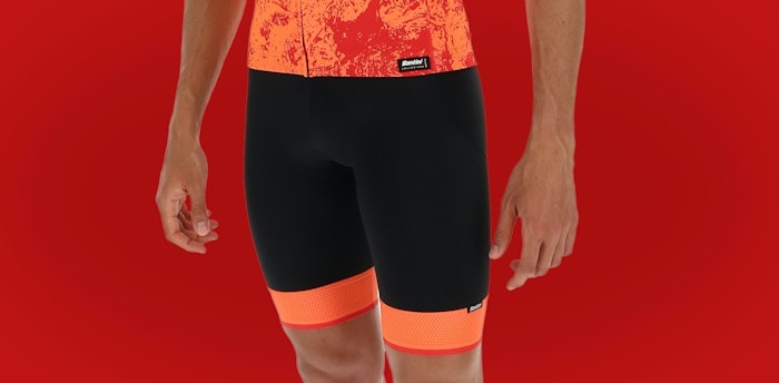 Close-up of person wearing black and orange Scatto bib shorts against a red background.