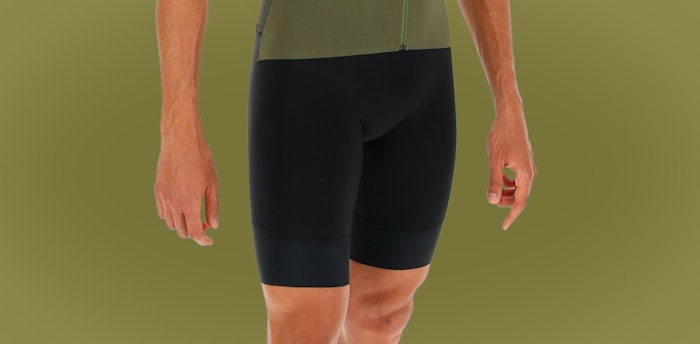 Close-up of person wearing black Genio bib shorts against an olive green background.