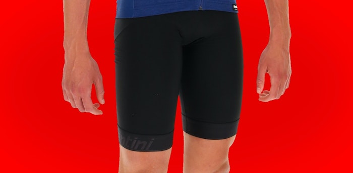 Close-up of person wearing black Mago 2.0 bib shorts against a red background.
