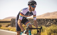 Cyclist riding a bike on a sunny road wearing a colorful striped cycling jersey.