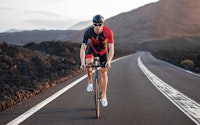 Cyclist riding on a long, deserted road with mountains in the background.