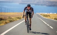 Cyclist riding on an open road with a scenic ocean view in the background.