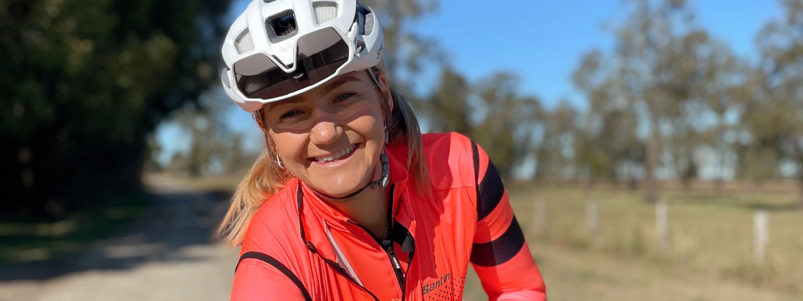 Smiling cyclist in a white helmet and bright orange Santini cycling jacket.